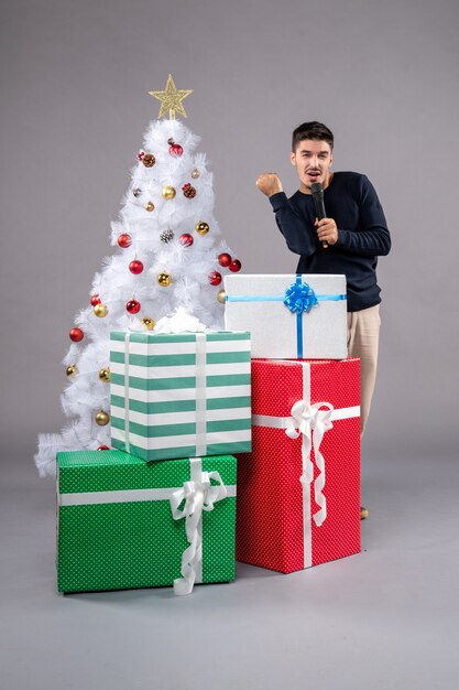 Vue de face jeune homme tenant un micro avec des cadeaux sur le gris