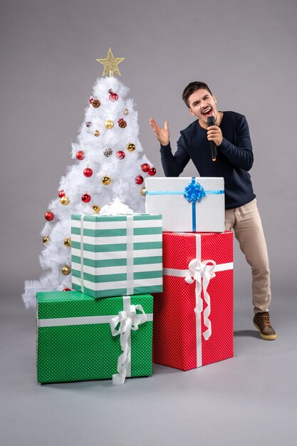 Vue de face jeune homme tenant un micro avec des cadeaux sur le gris