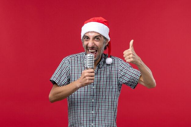 Vue de face jeune homme tenant le microphone sur la musique de chanteur de vacances émotions mur rouge