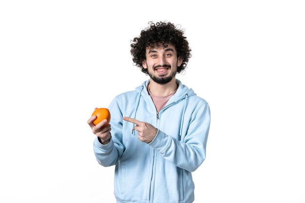 Vue de face jeune homme tenant une orange fraîche sur une surface blanche