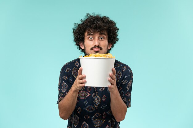 Vue de face jeune homme tenant panier avec cips sur le fond bleu film cinéma cinéma cinéma à distance