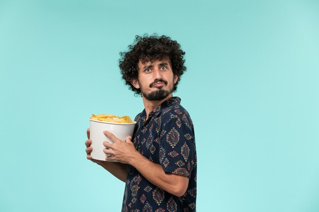 Vue de face jeune homme tenant panier avec cips sur un mur bleu clair cinéma cinéma cinéma cinéma à distance