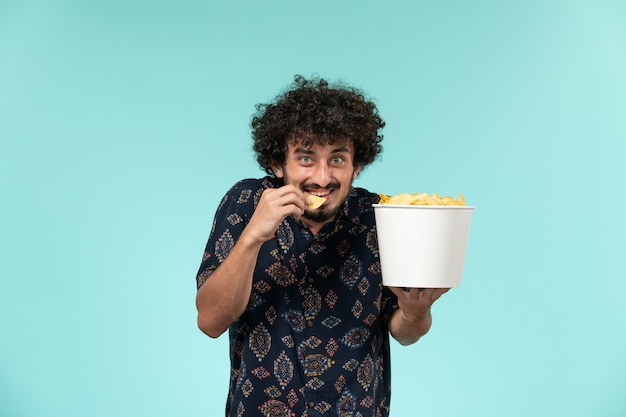 Photo gratuite vue de face jeune homme tenant un panier avec des cips de pommes de terre et les manger sur le mur bleu cinéma cinéma cinéma mâle