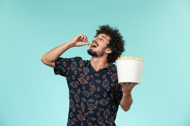 Vue de face jeune homme tenant un panier avec des cips de pommes de terre et manger sur le mur bleu cinéma films cinéma mâle