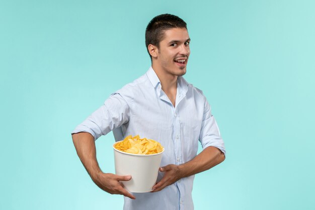 Vue de face jeune homme tenant un panier avec des cips de pommes de terre sur un mur bleu cinéma à distance lonely male male