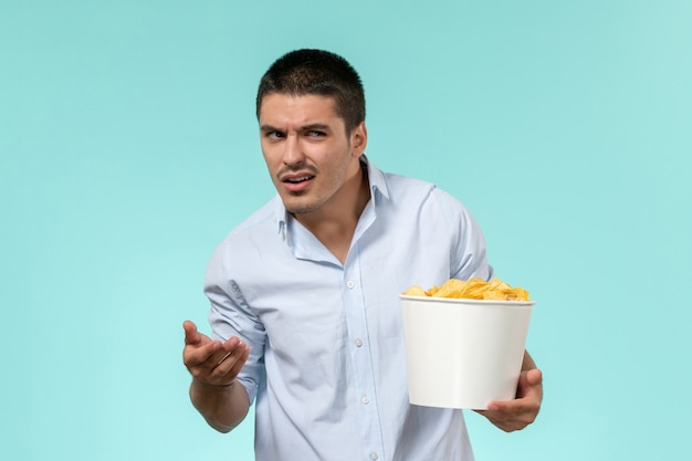 Vue de face jeune homme tenant un panier avec des cips de pommes de terre sur le mur bleu clair cinéma cinéma à distance mâle solitaire