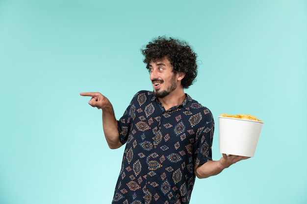 Vue de face jeune homme tenant un panier avec des cips de pommes de terre sur le mur bleu des films de cinéma à distance