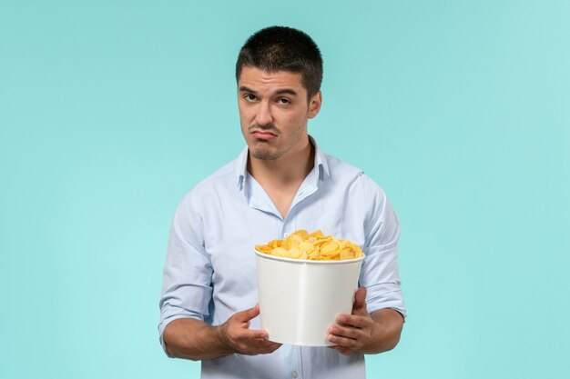 Vue de face jeune homme tenant un panier avec des cips de pommes de terre sur un mur bleu lonely remote male films cinema