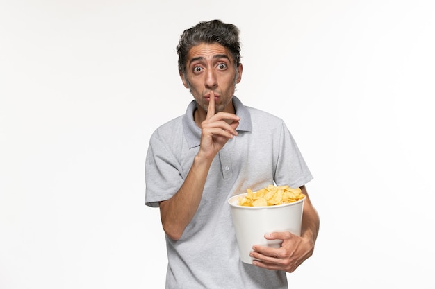 Vue de face jeune homme tenant le panier avec des croustilles sur un bureau blanc