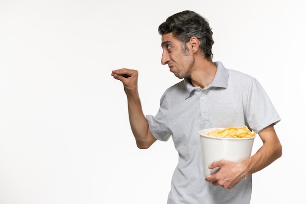 Vue de face jeune homme tenant le panier avec des croustilles de parler à quelqu'un sur une surface blanche