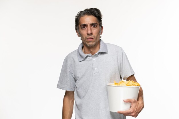 Vue de face jeune homme tenant le panier avec des croustilles sur une surface blanche légère