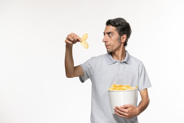 Vue de face jeune homme tenant le panier avec des croustilles sur une surface blanche