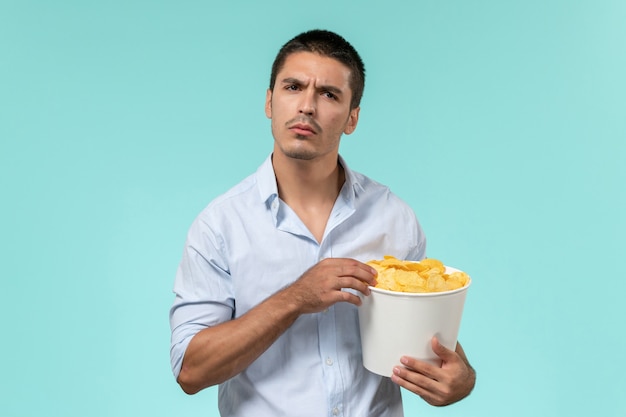 Vue de face jeune homme tenant un panier avec des morceaux de pommes de terre et regarder un film sur un mur bleu clair cinéma cinéma à distance