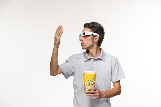 Vue de face jeune homme tenant le paquet de pop-corn en d lunettes de soleil sur un bureau blanc