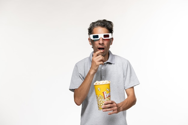 Vue de face jeune homme tenant le paquet de pop-corn en d lunettes de soleil sur la surface blanche