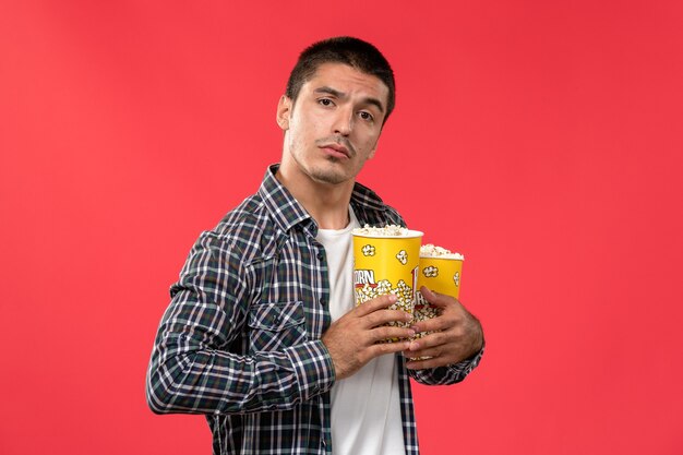 Vue de face jeune homme tenant des paquets de pop-corn sur le mur rouge clair cinéma cinéma film cinéma