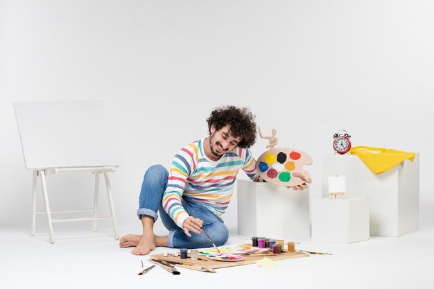 Vue De Face D'un Jeune Homme Tenant Des Peintures Et Un Gland Pour Dessiner Sur Un Mur Blanc
