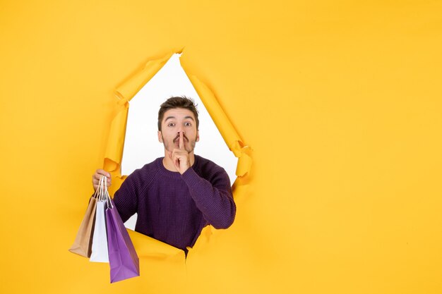 Vue de face jeune homme tenant de petits paquets après avoir fait du shopping sur un fond jaune cadeau nouvel an présent vacances de couleur de noël