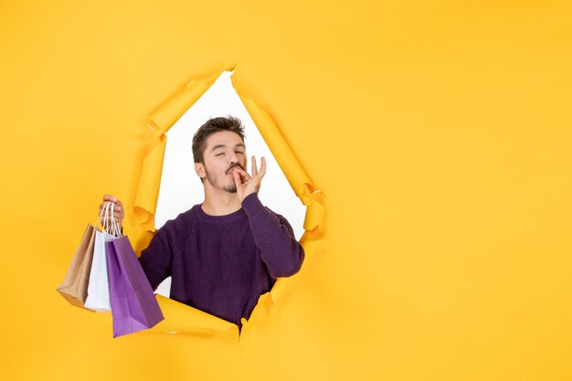 Vue de face jeune homme tenant de petits paquets après le shopping sur fond jaune modèle cadeau nouvel an présent couleur de noël