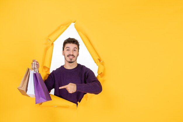 Vue de face jeune homme tenant de petits paquets après le shopping sur fond jaune modèle cadeau nouvel an présent couleur de noël