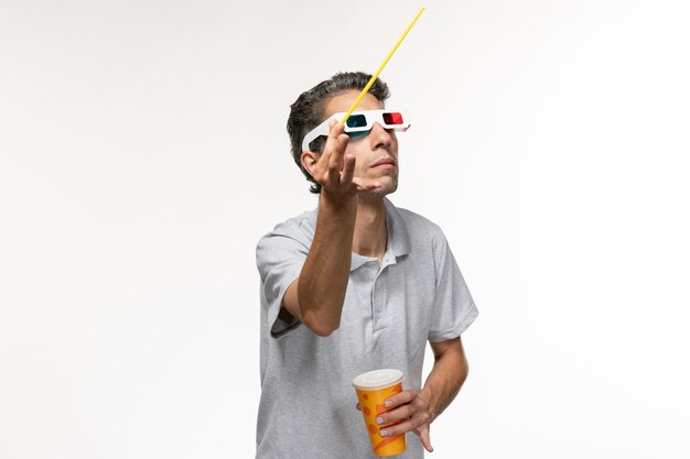 Vue de face jeune homme tenant un soda et regarder un film dans des lunettes de soleil sur un bureau blanc