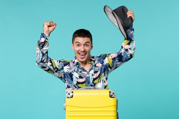 Vue de face jeune homme tenant son chapeau et se préparant pour le voyage se sentant excité sur l'espace bleu