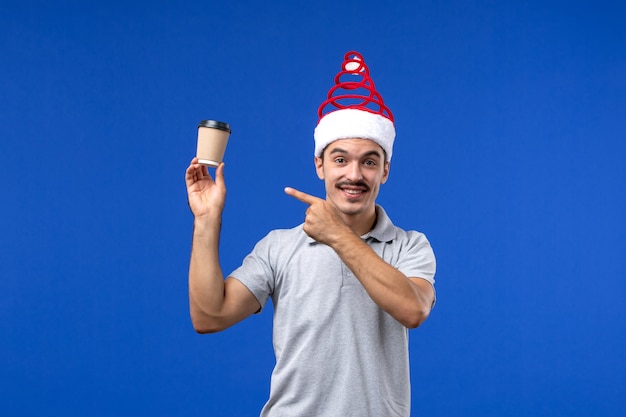 Vue de face jeune homme tenant une tasse de café en plastique sur le mur bleu vacances hommes nouvel an