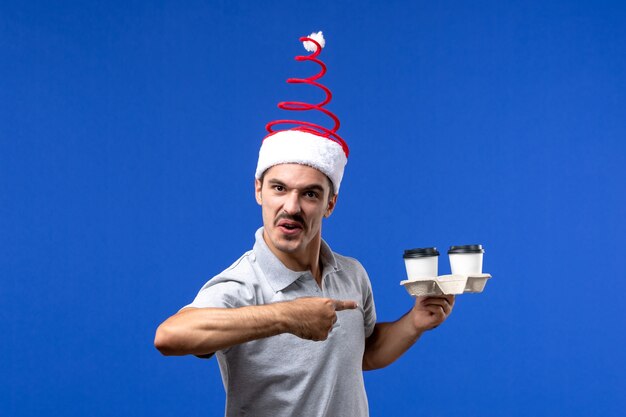 Vue de face jeune homme tenant des tasses de café sur le plancher bleu émotion mâle nouvel an