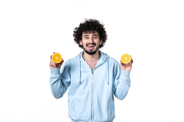 Vue de face jeune homme tenant des tranches d'orange fraîches sur blanc