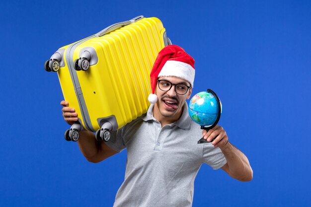 Vue de face jeune homme transportant un sac jaune sur les avions mur bleu voyage de vacances mâle