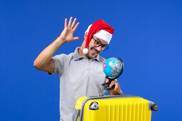 Vue de face jeune homme transportant un sac jaune avec globe sur mur bleu voyage de vacances avions