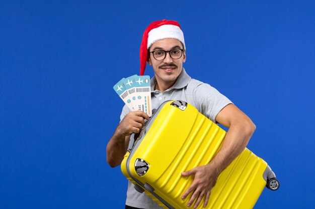 Vue de face jeune homme transportant un sac lourd avec des billets sur l'avion de vacances de vol de mur bleu