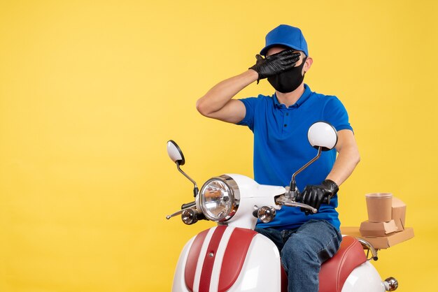 Vue de face jeune homme en uniforme bleu sur fond jaune covid- pandemic service job virus travail vélo