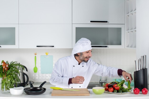 Vue de face jeune homme en uniforme prenant des légumes de la table