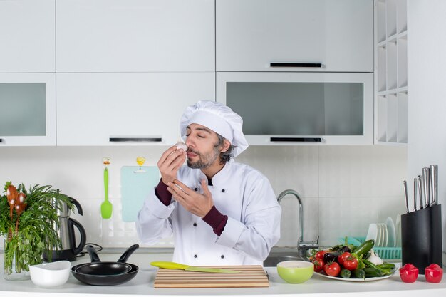 Vue de face jeune homme en uniforme sentant l'ail dans la cuisine