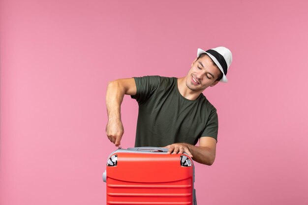 Vue de face jeune homme en vacances avec sac rouge sur un bureau rose