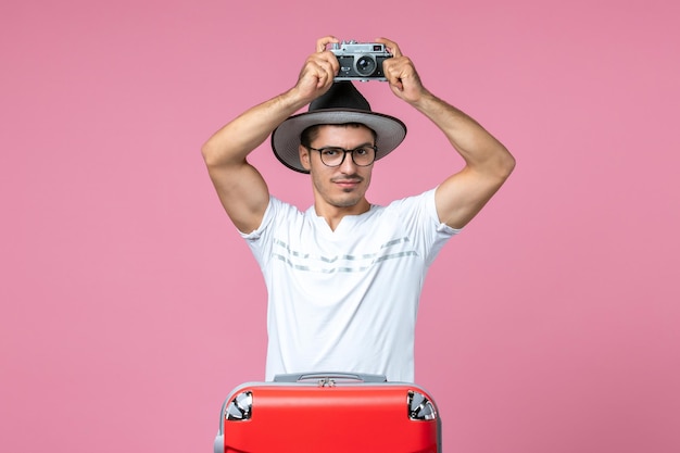 Photo gratuite vue de face d'un jeune homme en vacances avec un sac tenant un appareil photo prenant des photos sur le mur rose