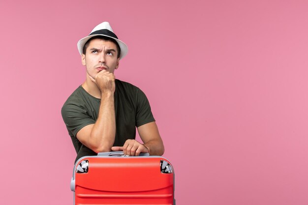 Vue de face jeune homme en vacances avec son sac rouge pensant à l'espace rose