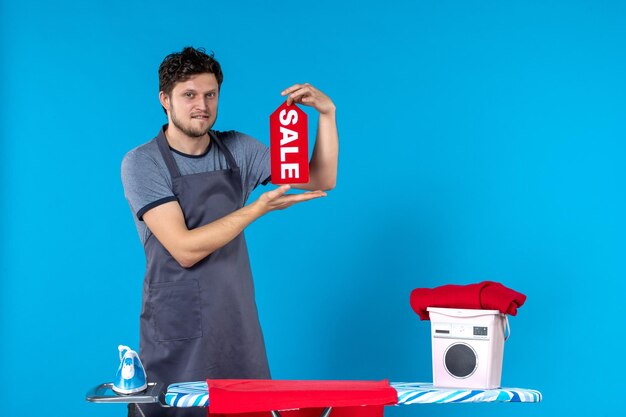 Vue de face jeune homme avec vente écrit dans ses mains sur une surface bleue