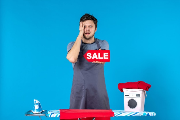 Vue de face jeune homme avec vente rouge écrit dans ses mains sur la surface bleue