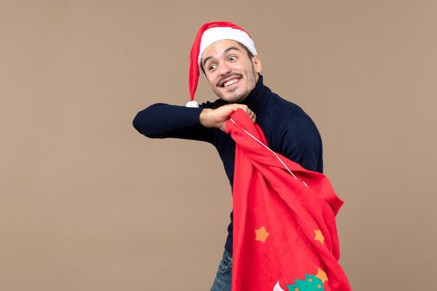 Vue de face jeune homme vérifiant le sac présent rouge sur fond marron vacances de Noël santa