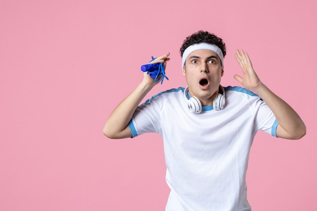 Vue de face jeune homme en vêtements de sport avec corde à sauter sur le mur rose