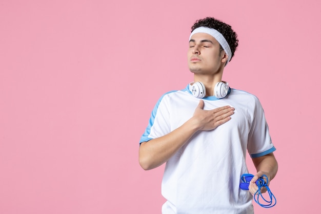 Vue de face jeune homme en vêtements de sport avec corde à sauter sur le mur rose