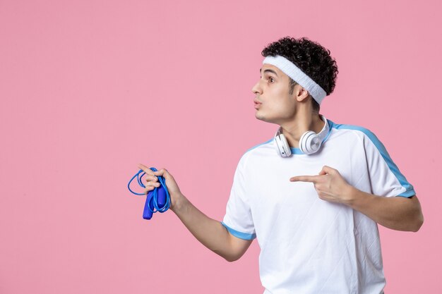 Vue de face jeune homme en vêtements de sport avec corde à sauter sur le mur rose