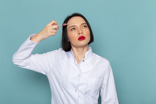 Une vue de face jeune infirmière en costume médical blanc injectiong elle-même sur le médecin de l'hôpital de médecine de bureau bleu