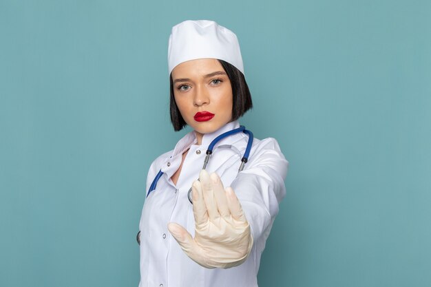 Une vue de face jeune infirmière en costume médical blanc et stéthoscope bleu montrant le panneau d'arrêt sur le médecin de l'hôpital de médecine de bureau bleu