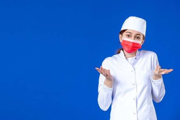 Vue de face de la jeune infirmière en costume médical avec masque rouge sur bleu