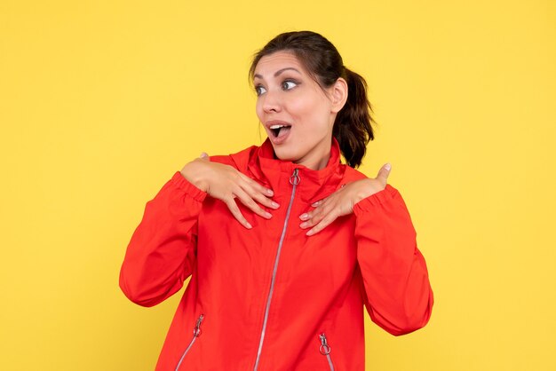 Vue de face jeune jolie femme en manteau rouge sur fond jaune