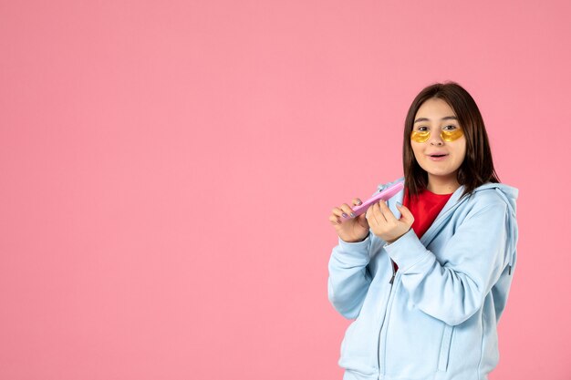 Vue de face jeune jolie femme avec des patchs oculaires faisant ses ongles sur fond rose