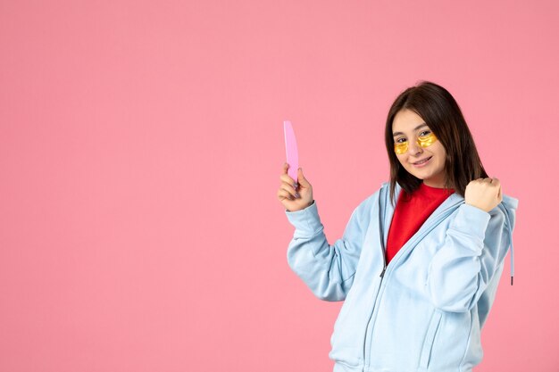 Vue de face jeune jolie femme avec patchs oculaires et lime à ongles sur fond rose